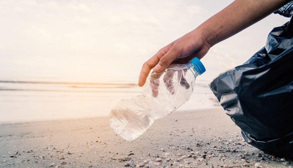 person picking up plastic water bottle on beach