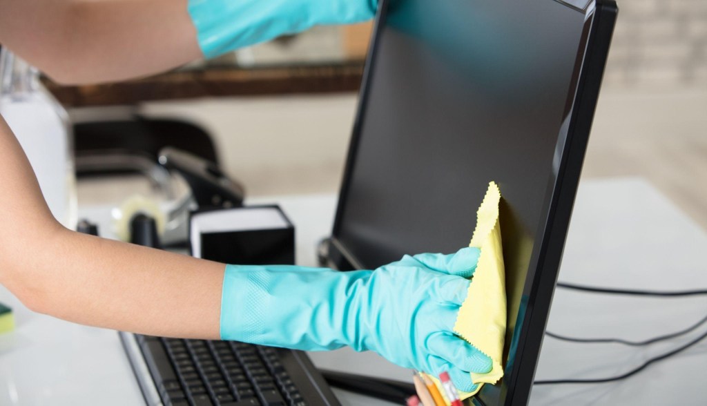 person sanitizing desktop computer