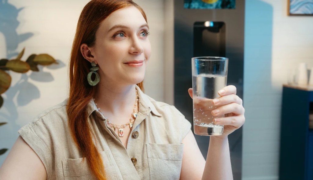 Woman with red hair looking up with a glass of water in hand and Twist water dispenser in the background