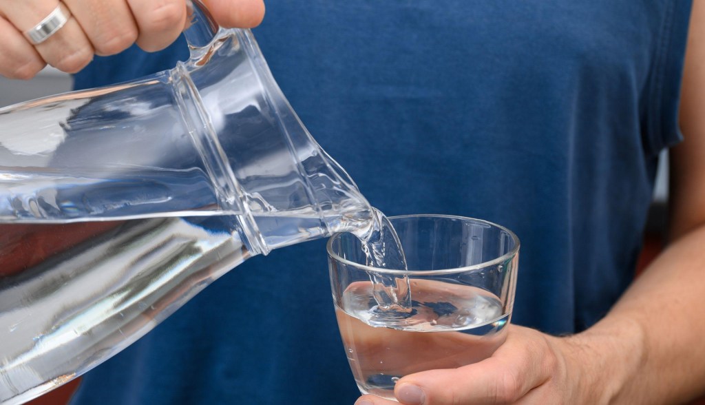 person pouring water from pitcher into glass