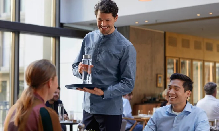 Server at restaurant serving bottle of water to table