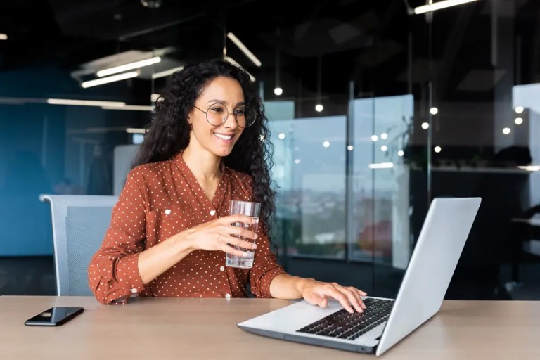 woman smiling working at desk holding glass of water