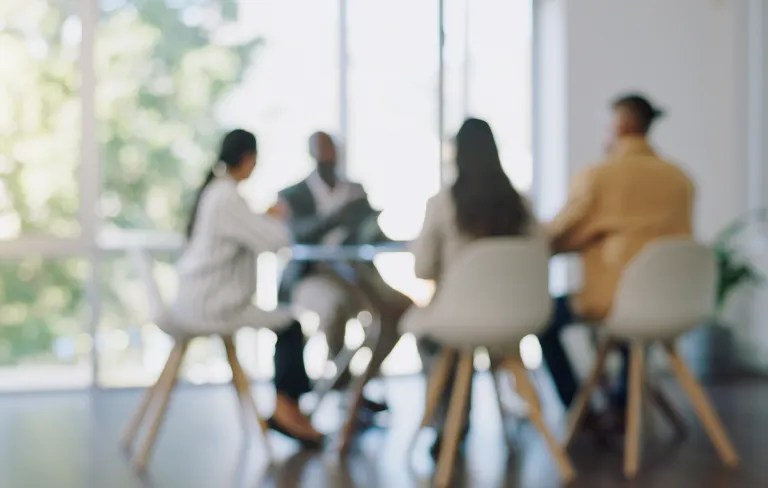 blurry image of workers in the office sitting at a conference room