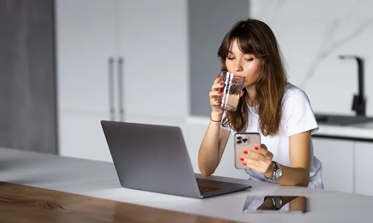 woman at counter with laptop drinking water