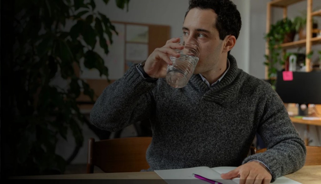 Man with gray sweater drinking water at work