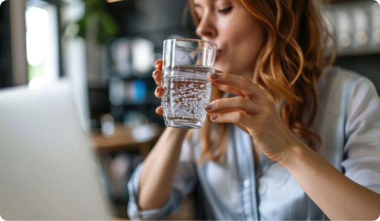 blond woman drinking sparkling water in front of computer