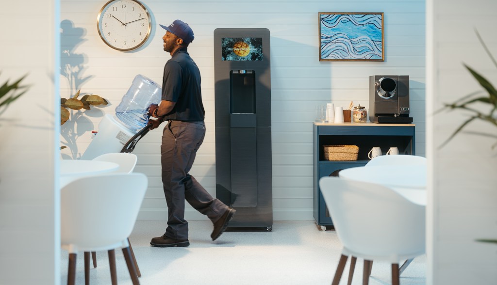 Man rolls out water delivery jug from office with Twist Water dispenser in the background