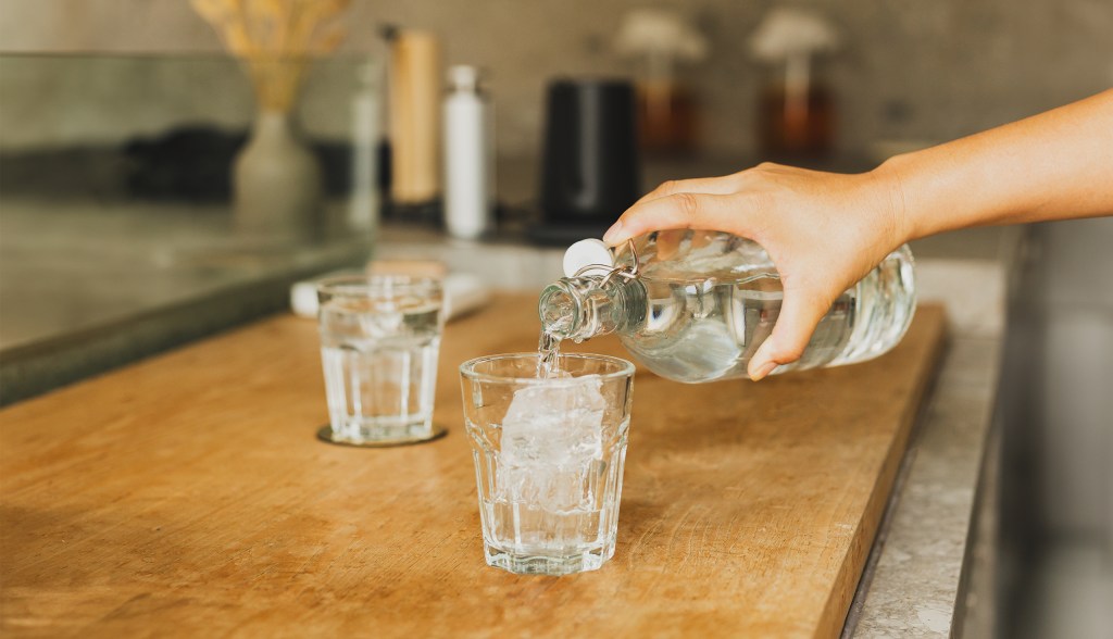 hand pouring water into glass of ice on wooden table