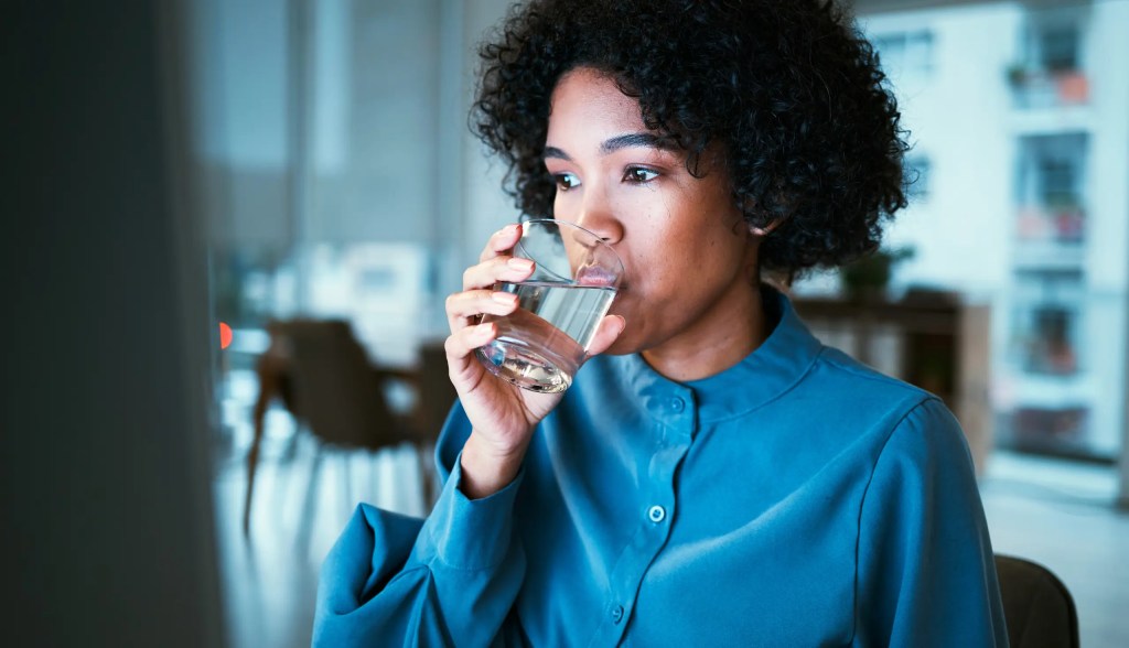 Woman in blue blouse drinking water at her computer