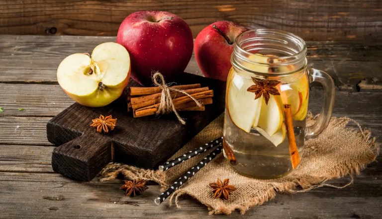 apple water with three apples behind and a cutting board next to it