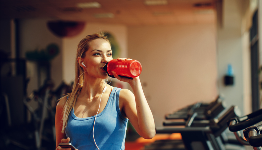 Woman drinking water in gym in front of treadmills